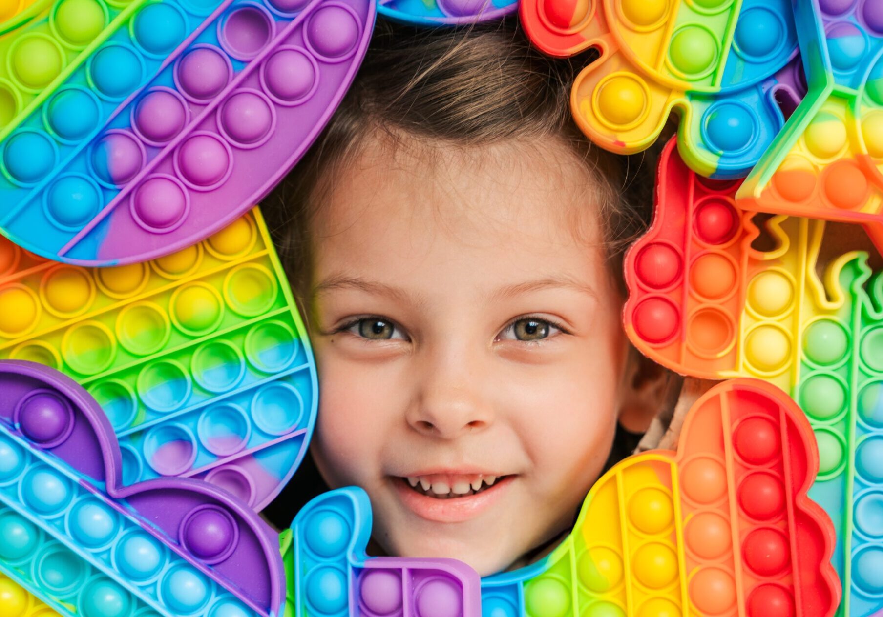 Little girl,kid,child head among many,lots of colorful pop it. Children play. Trendy silicone antistress colorful sensory push toy popit. Flapping fidget. Rainbow color.Cure of autism.Stress reliever.