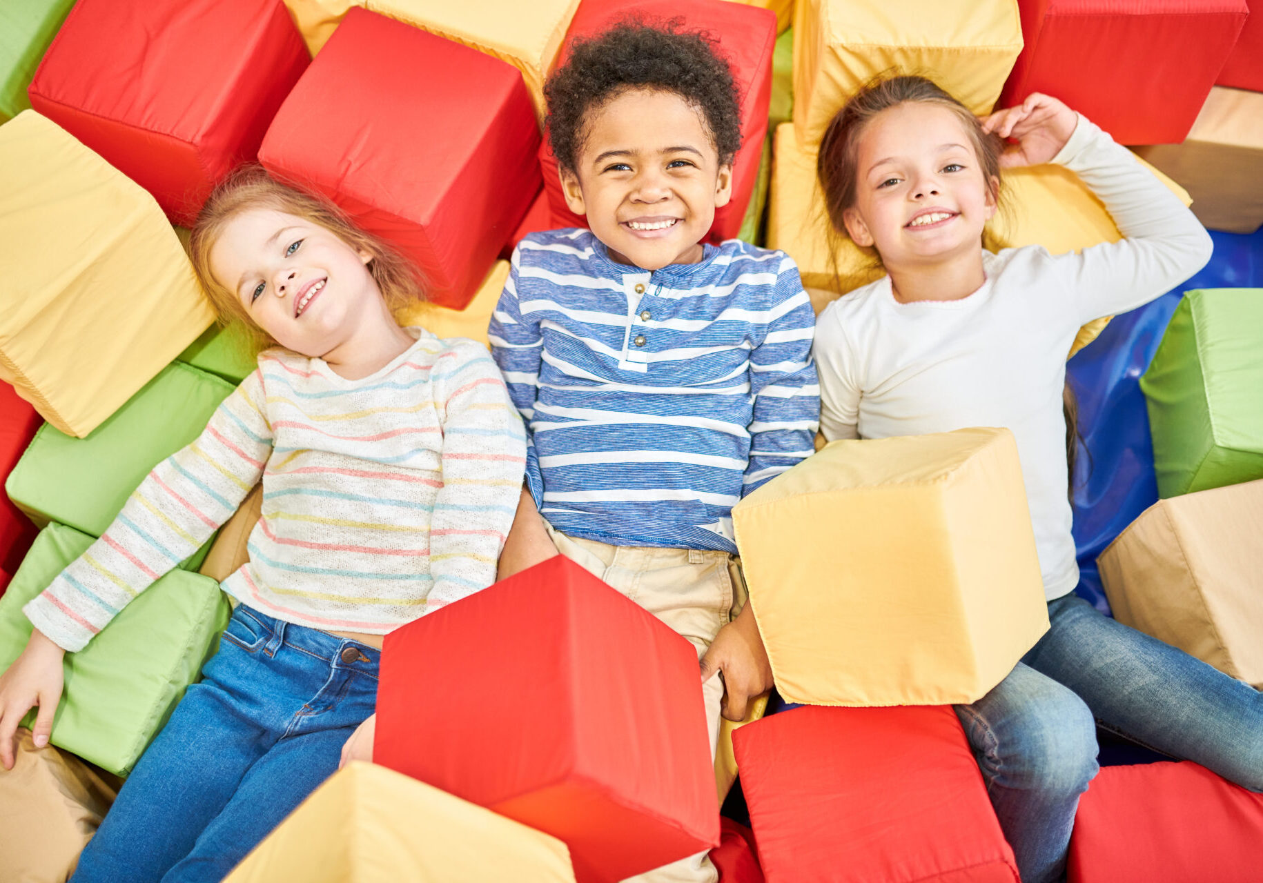 Colorful above view portrait of three happy little kids playing in foam pit of trampoline center, copy space